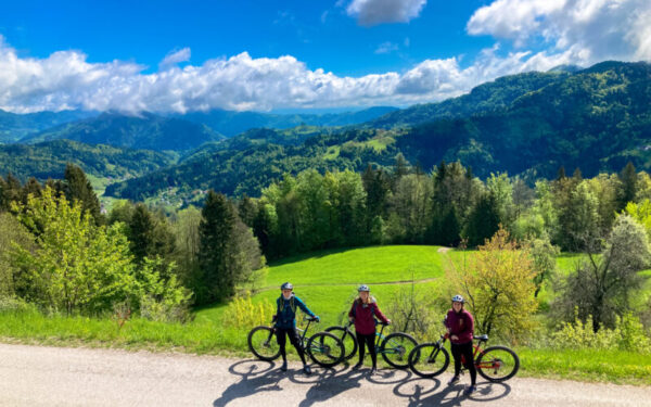 Three ladies stand proudly with their bikes, smiling as they pause to take in the breathtaking view.